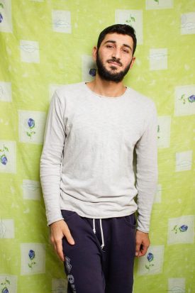 Portrait of refugee Abdoulah standing against a green background