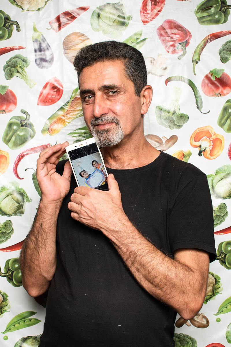 Portrait of Syrian Bassil Watti holding a phone showing photos of his children