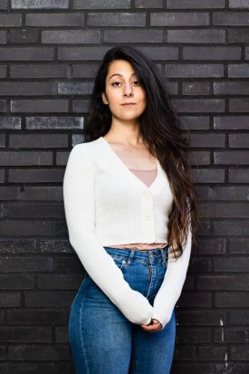 Portrait of Refugee Shatoo Amin in white against a black brick wall