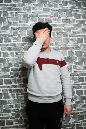 Portrait of Refugee Haroon Alemjaar hiding his face