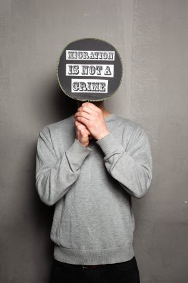 Portrait of refugee holding a card saying 'Migration is not a crime' that hides their face