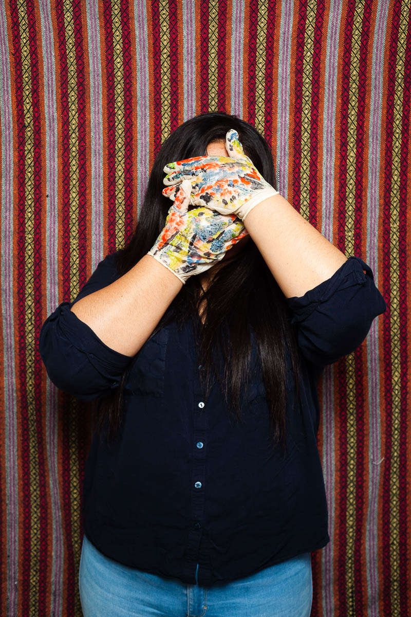 Portrait of refugee Lia hiding her face with her hand wearing painted gloves