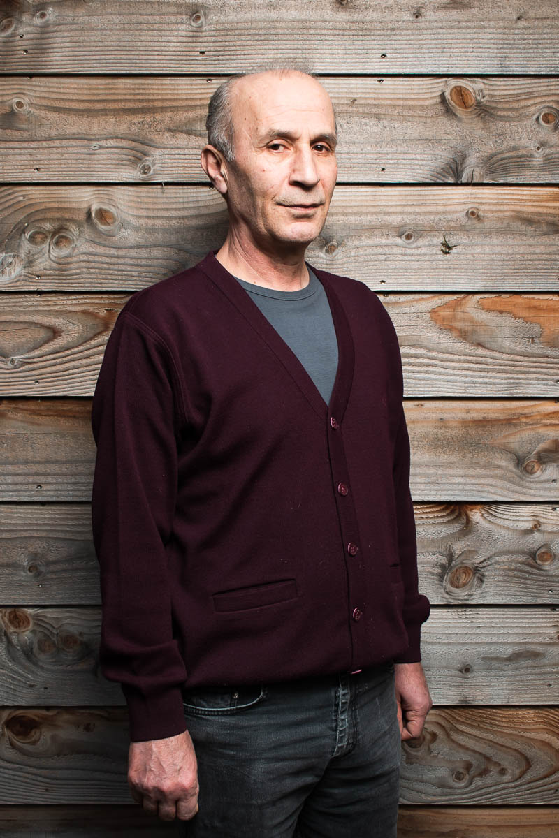 Portrait of refugee Mehmet standing against a wooden plan background