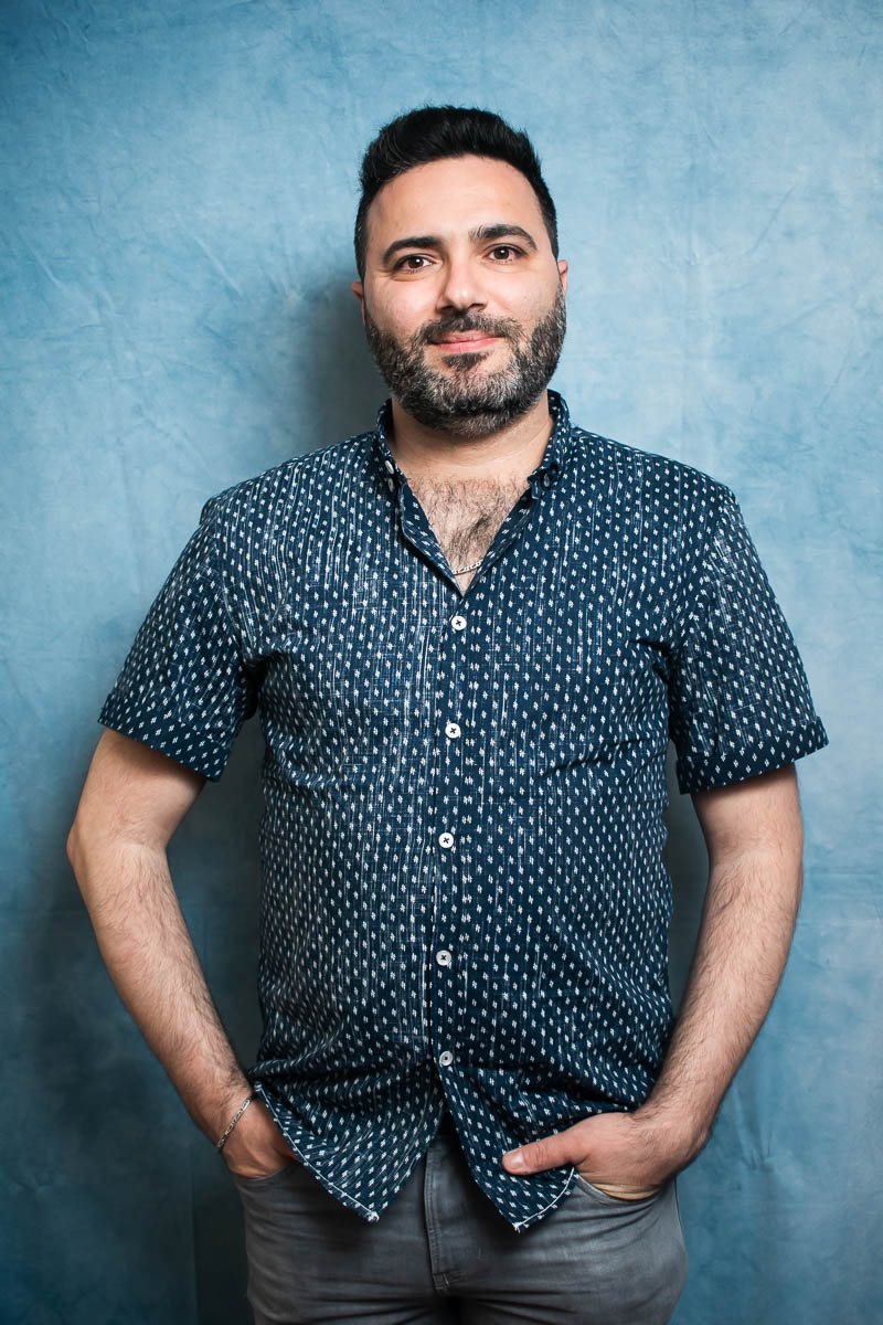 Portrait of refugee Adel Al Nabelsi with hands in pocket against a blue background