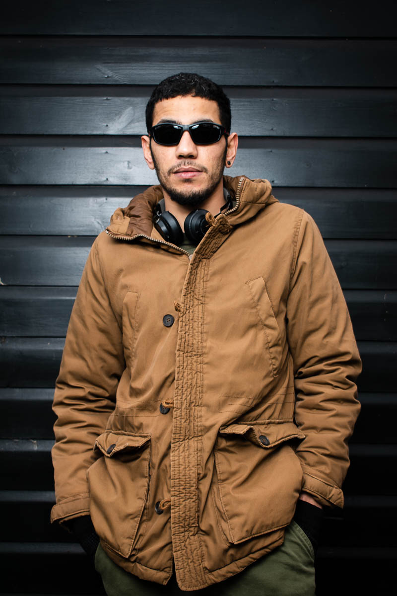 Portrait of refugee Emad wearing sunglasses and a trench coat