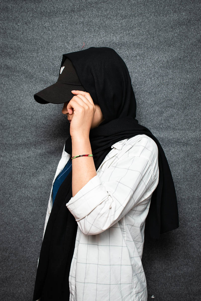 Portrait of refugee Rasta wearing a hijab and hiding her face with her cap
