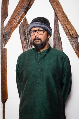 Portrait of refugee Athul Pereira wearing a beanie cap against a painted background