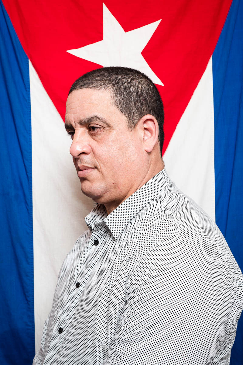 Portrait of refugee Pavel's side profile standing in front of the Cuban flag