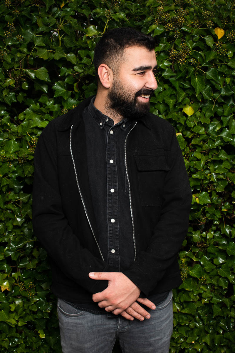 Portrait of refugee Kadir looking to the side against a hedge