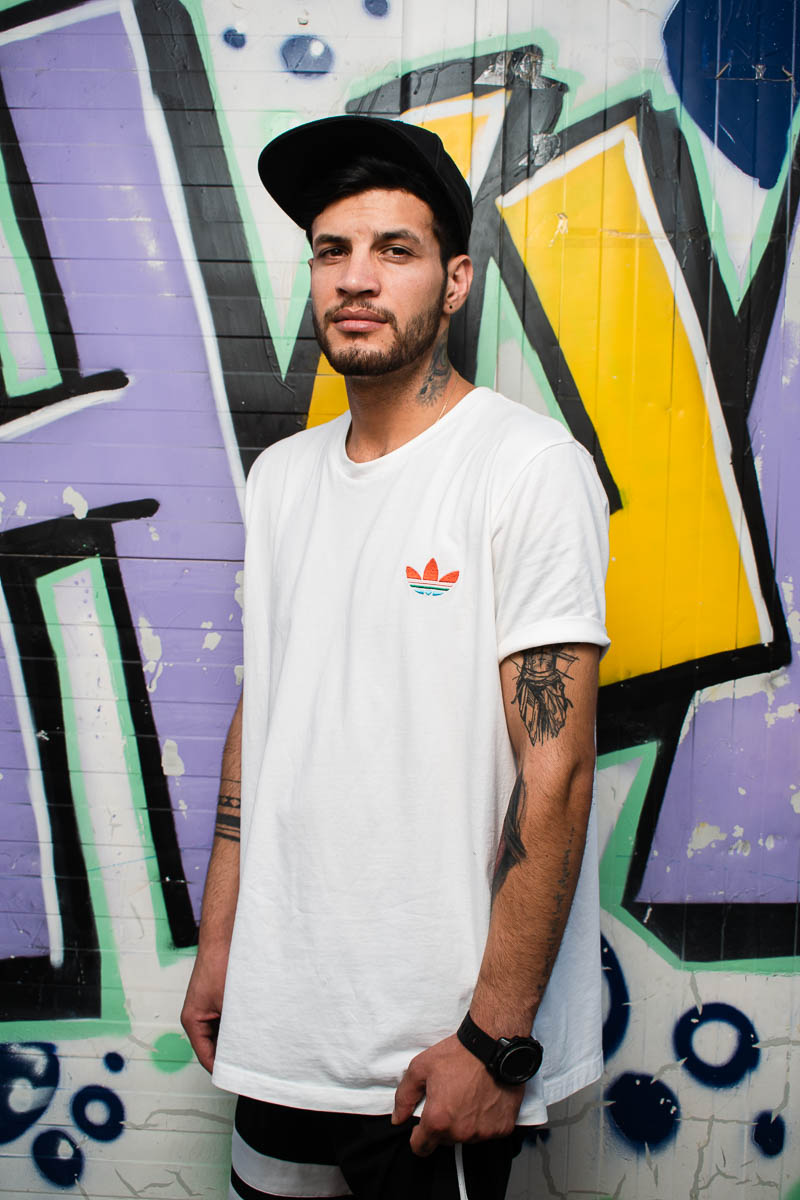 Portrait of refugee Omid against a graffiti wall wearing a snapback