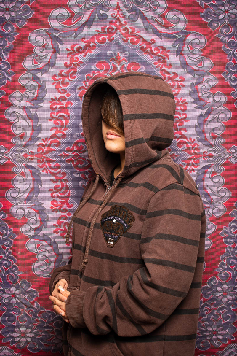 Portrait of refugee Nilofer in a hoodie with her face hidden by her hair