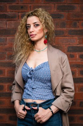 Portrait of refugee Berry standing against a brick wall