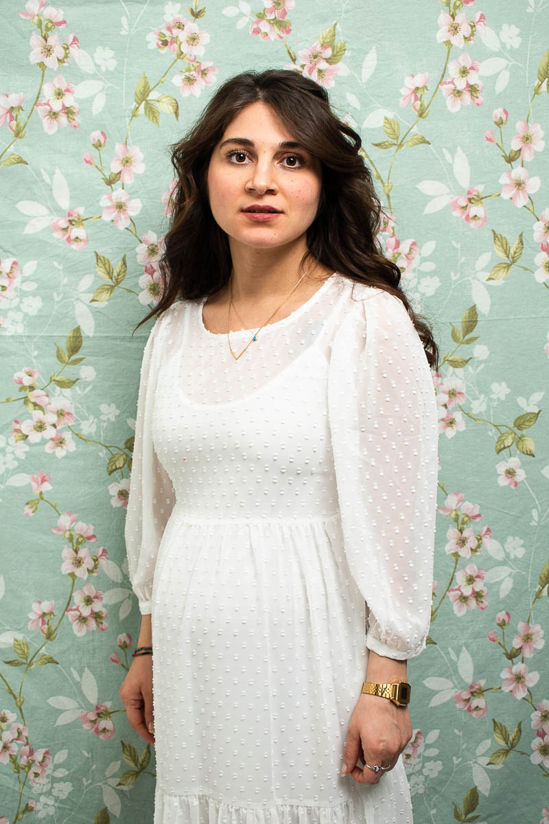 Portrait of refugee Laleş wearing a white dress against a floral wall