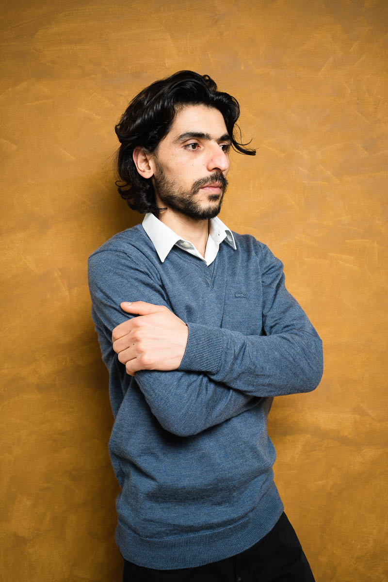 Portrait of refugee Hossein Hajizade holding his arms with a stern expression