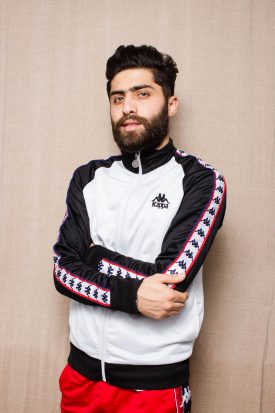 Portrait of refugee Safi with his arms folded across wearing a sweatshirt