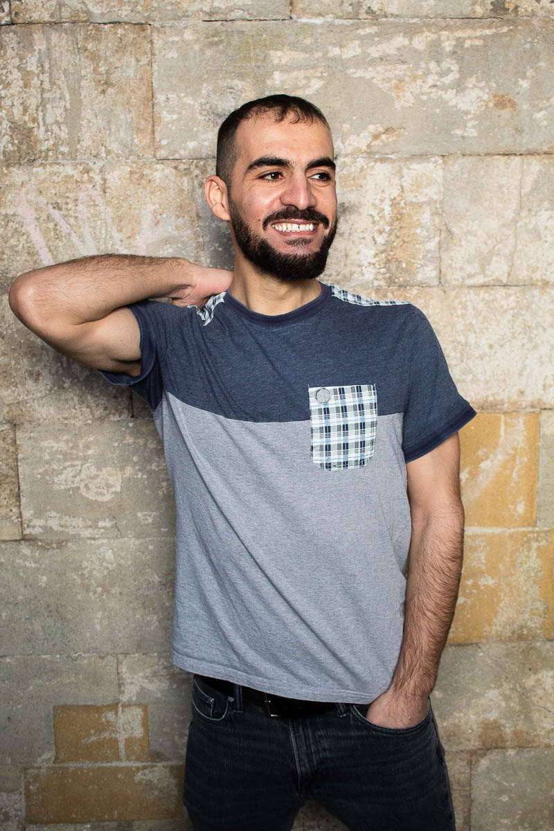 Portrait of refugee Renas smiling with one hand on his heck