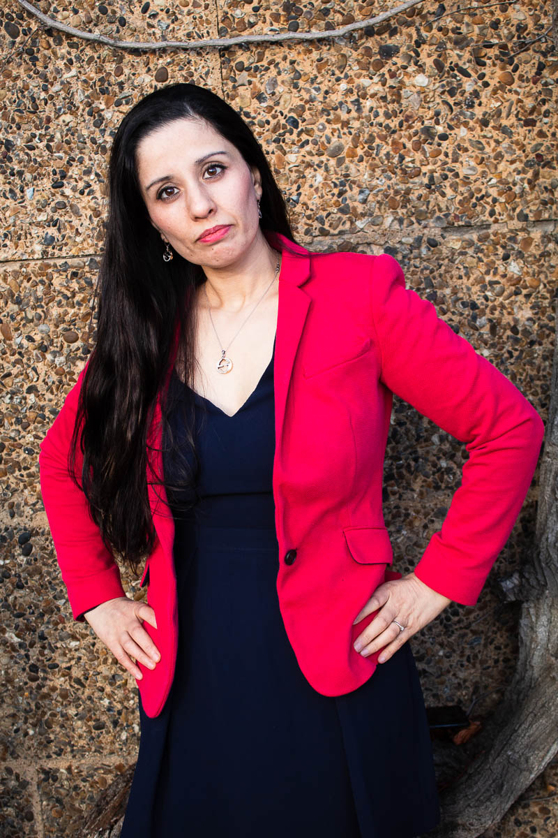 Portrait of refugee Bahar wearing a red blazer with her hands on her hips