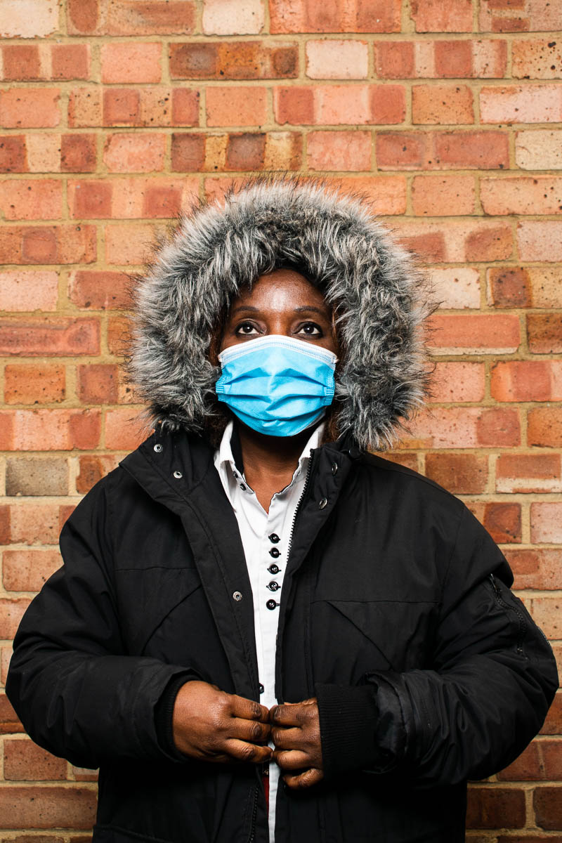 Portrait of refugee Francoise wearing a black parka and blue face mask