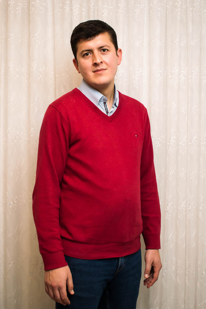 Portrait of refugee Mustafa wearing a red sweater vest