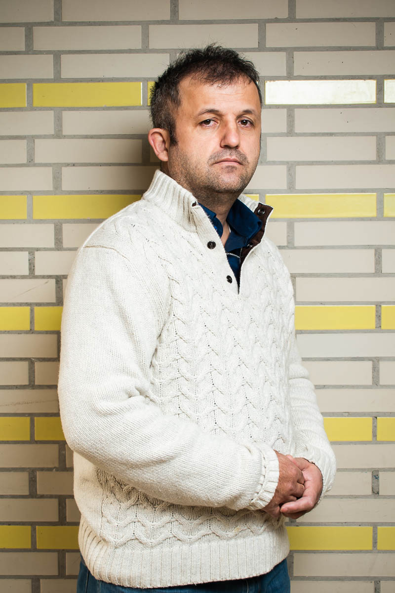 Portrait of refugee Nuri wearing a white sweater and holding his hands together