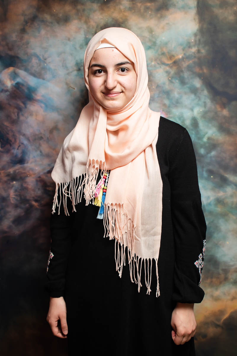 Portrait of refugee Razan wearing a peach coloured hijab smiling at the camera