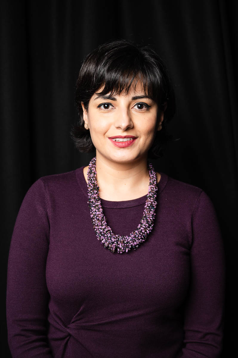 Portrait of refugee Tannaz wearing a big purple jewel necklace with a purple blouse