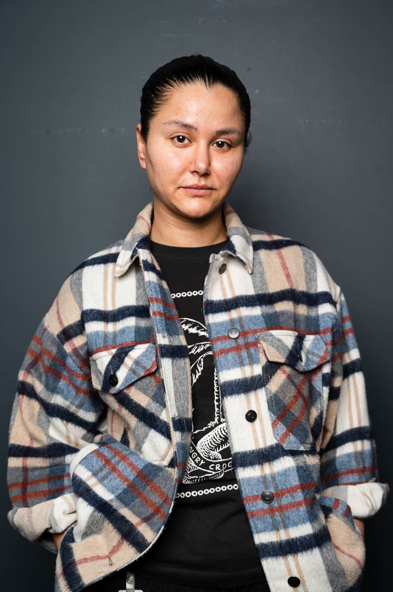 Portrait of refugee Hannah with her hands in the pocket of a checkered jacket she is wearing.