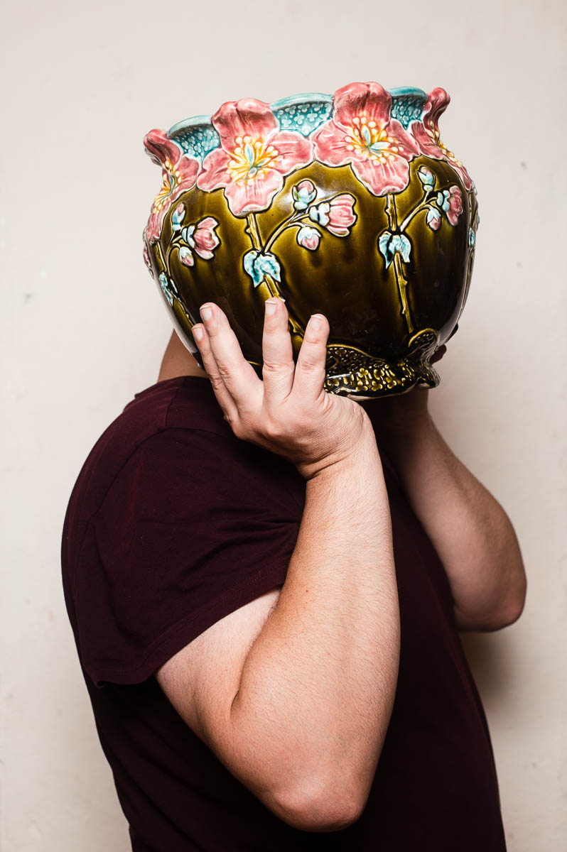 Portrait of refugee Ahmed standing sideways, hiding his face with a decorated vase