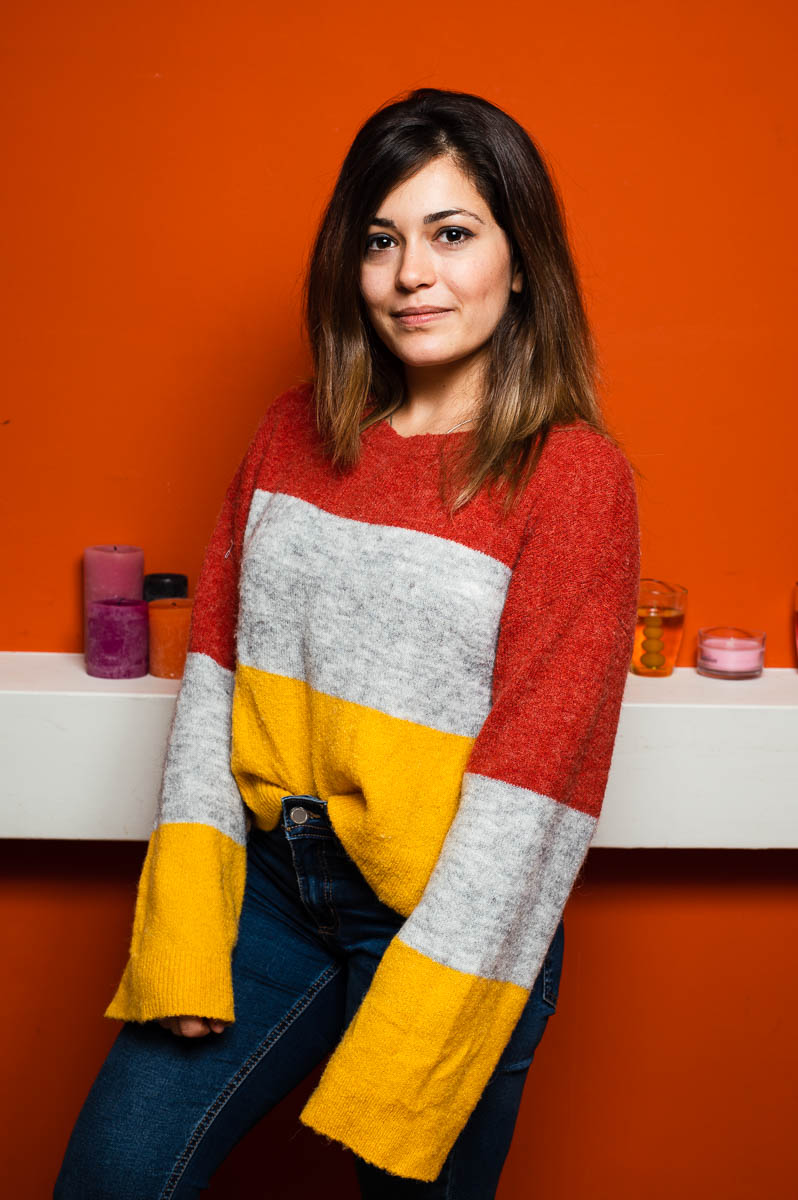 Portrait of refugee Leen wearing an oversized sweater against a red wall