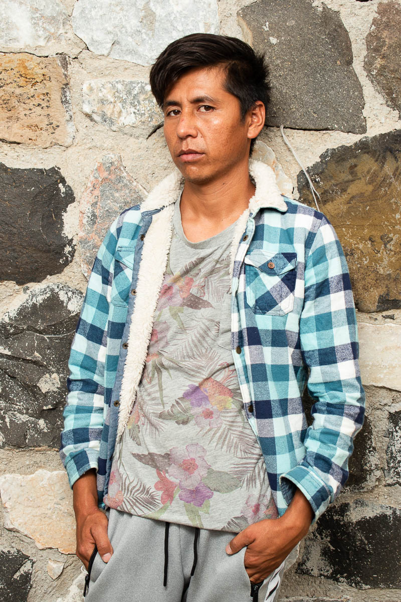 Portrait of refugee Nazar with hands in his pockets standing against a rock wall