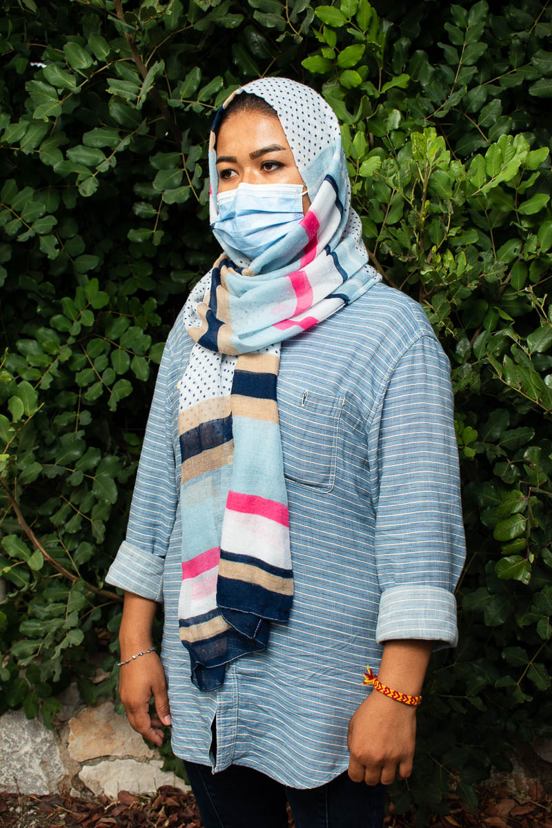 Portrait of refugee Shirin wearing a face mask against a green tree background