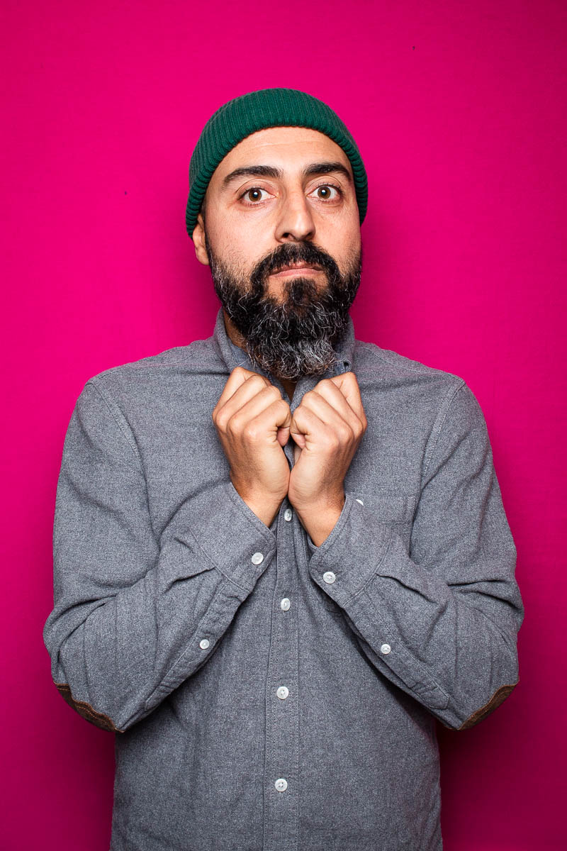 Portrait of refugee Yusef holding his hands to his chin against a pink background