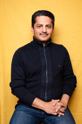 Portrait of refugee Ali sitting with his hands folded on his lap