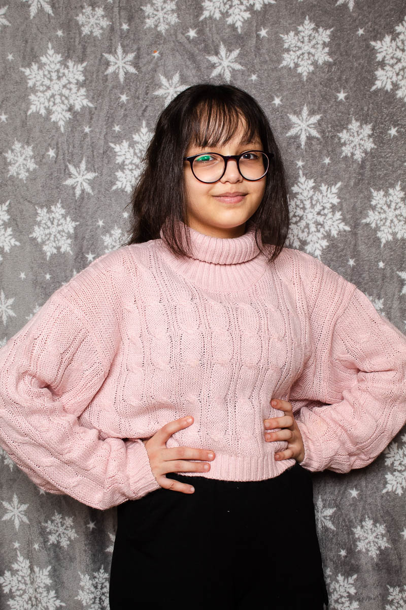 Portrait of refugee Gulia with her hands on her hips against a snowflake wallpaper