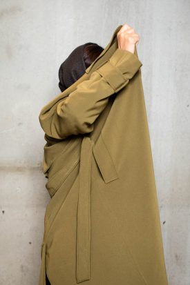 Portrait of refugee Sarah covering their face and body with a long coat