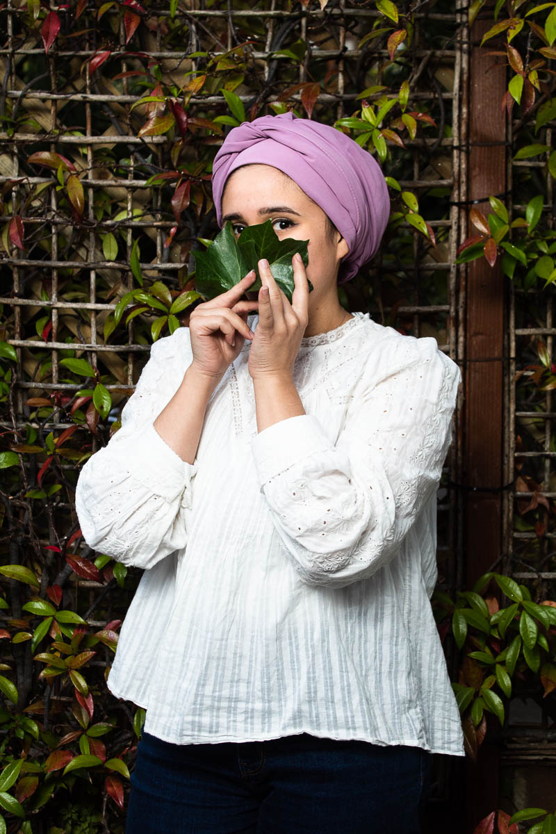 Portrait of refugee Nay wearing a pink turban hijab using a leaf to cover the lower half of her face