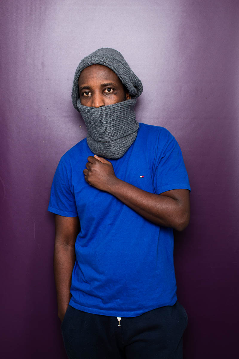 Portrait of refugee Binoyt wearing a woollen wrap across his head and mouth with his fisted hand held to the heart