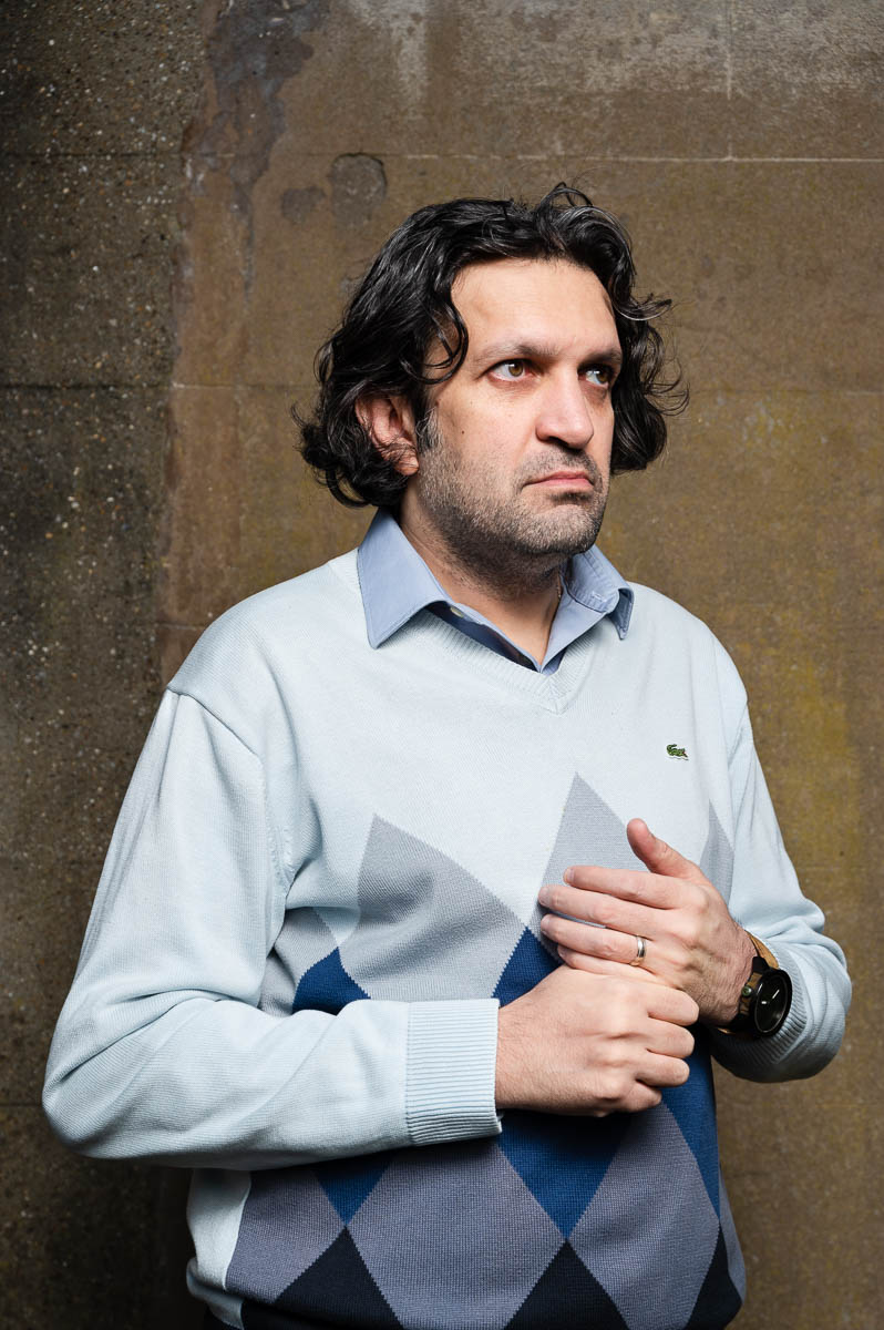 Portrait of refugee Kourosh wearing a sweater with a hand on his chest