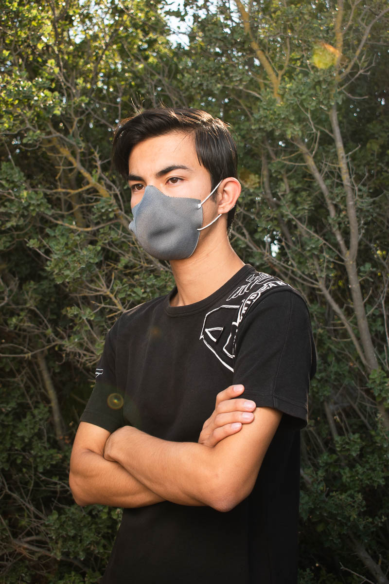 Portrait of refugee Amir with his arms folded wearing a grey face mask