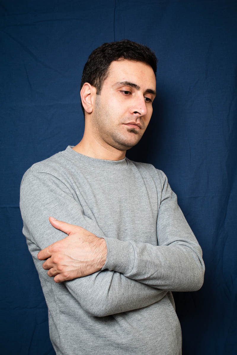 Portrait of refugee Aram with his arms folded looking down