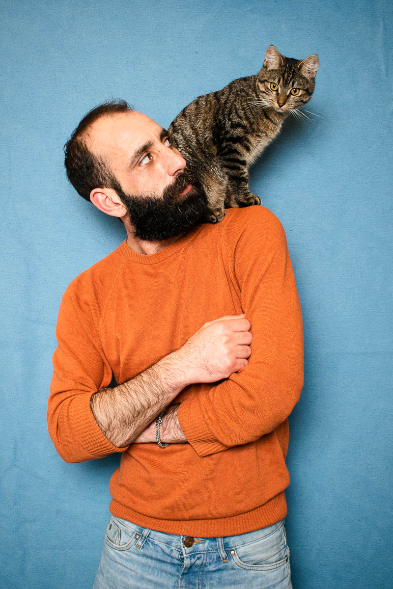 Portrait of refugee Hamid with his hands folded looking at the cat sitting on his shoulder