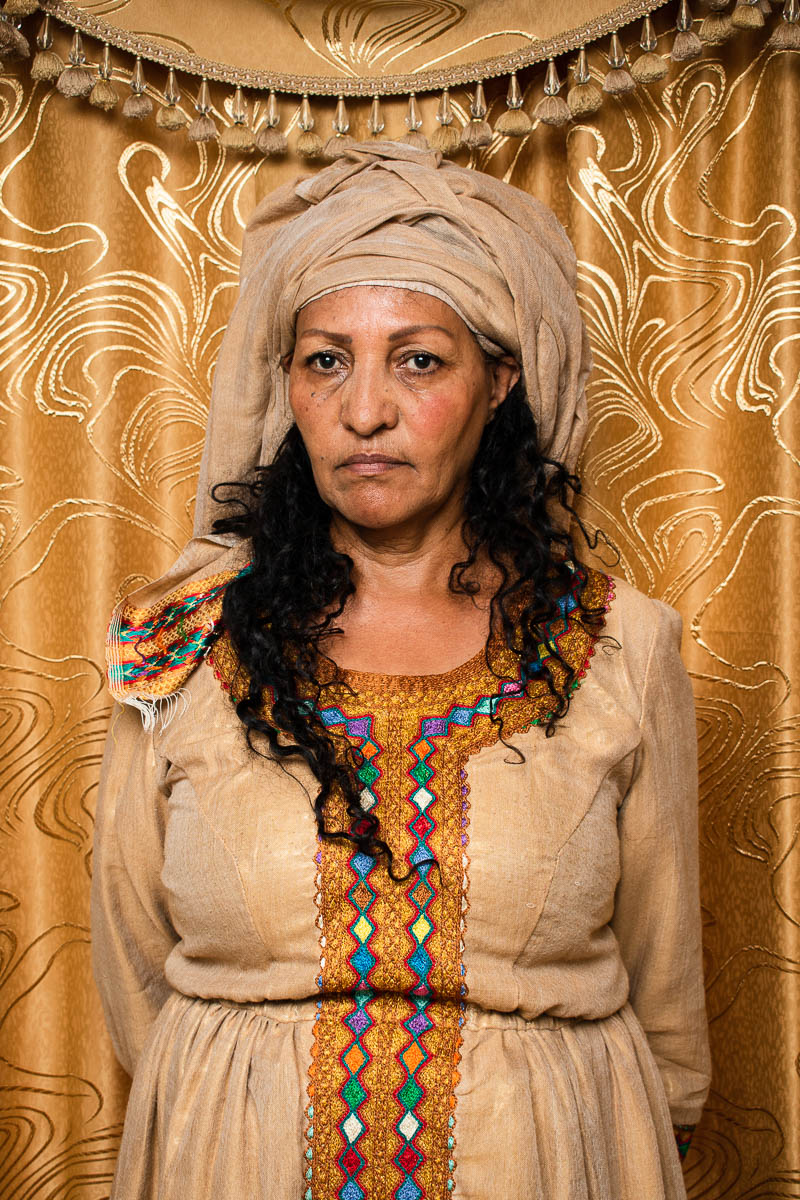 Portrait of refugee Elsa with her hands behind her back wearing a head turban