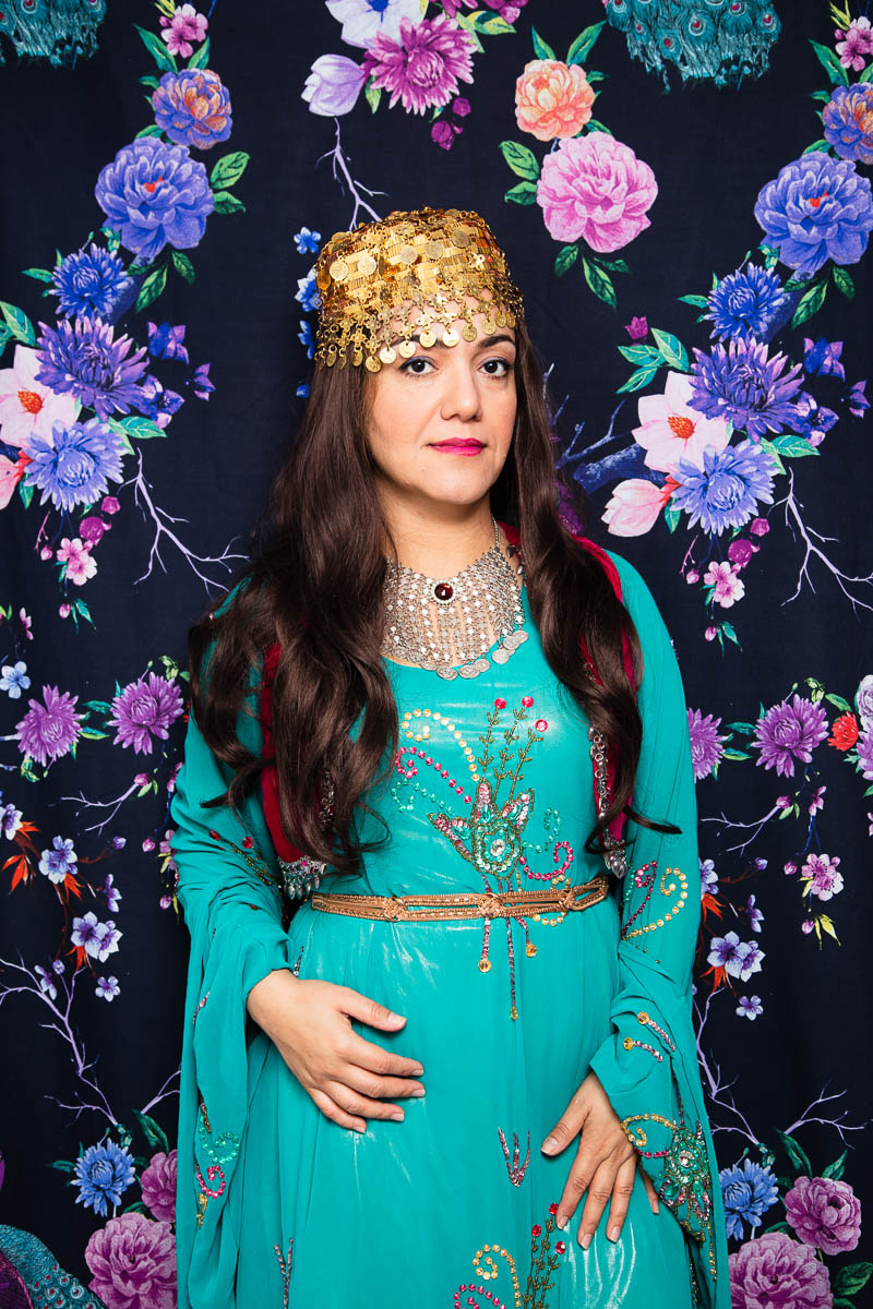 Portrait of refugee Tanya wearing a traditional blue Iraqi dress with a golden headpiece