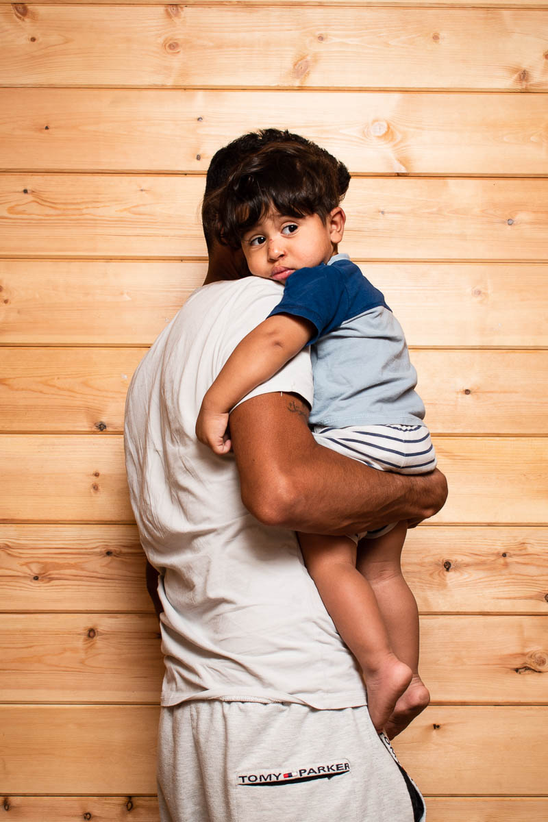 Portrait of refugee Ahmed with his face hidden by the child he is carrying in his arms