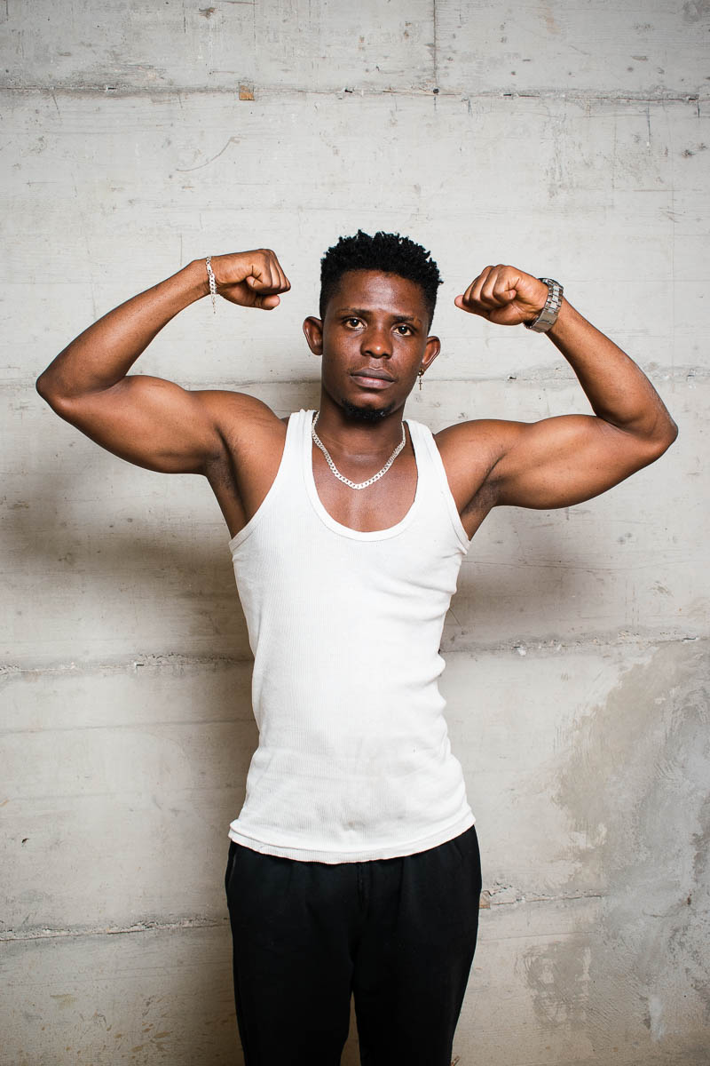 Portrait of refugee Tanguy with both his arms raised showing his biceps