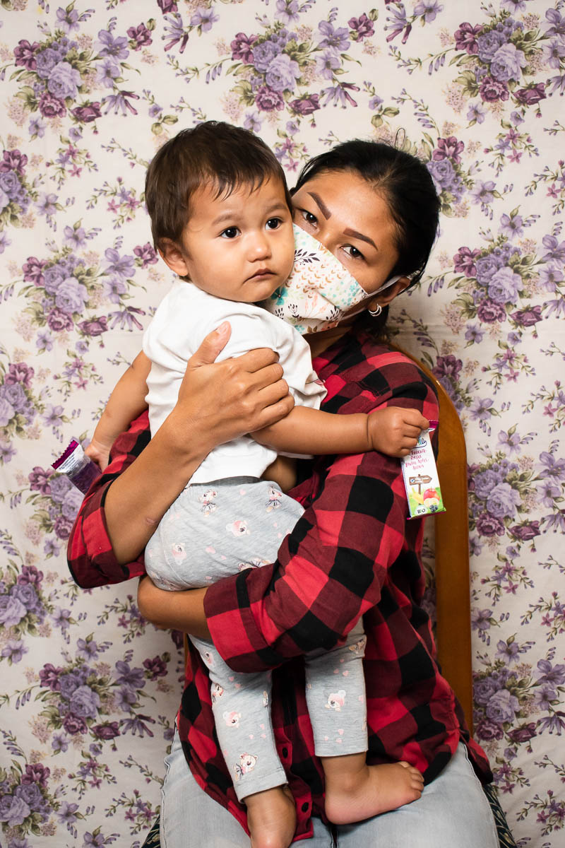 Portrait of refugee Yasaman wearing a face mask and carrying a child, hugging them close.