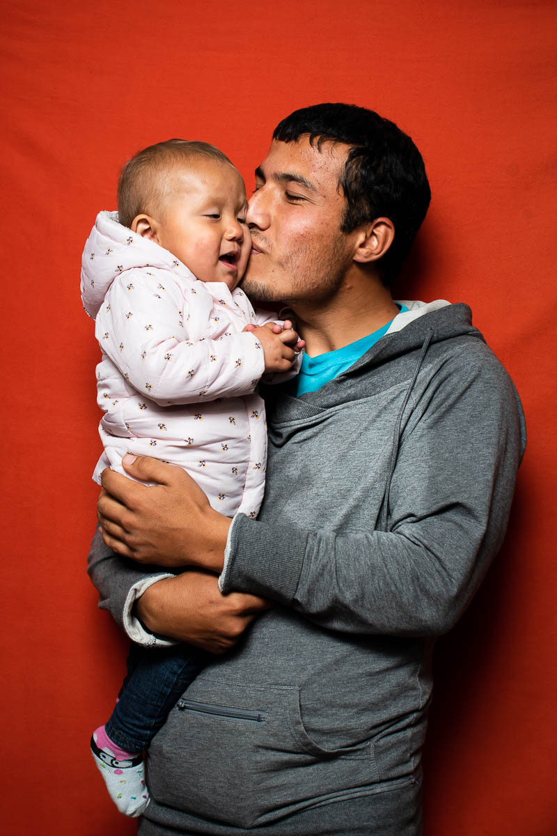 Portrait of refugee Nasrollah holding a baby and kissing their cheek