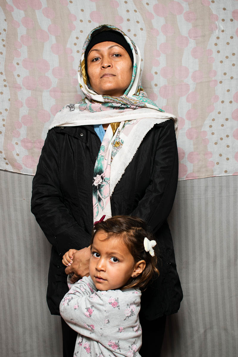 Portrait of refugee Amene with a lttle girl standing in front of her holding both her hands