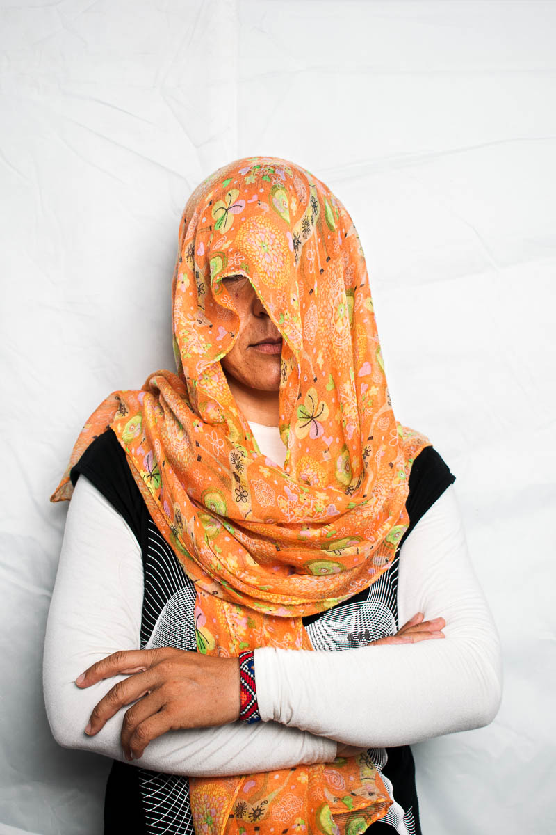 Portrait of refugee Mina with her hands folded, her head and face hidden with a floral scarf