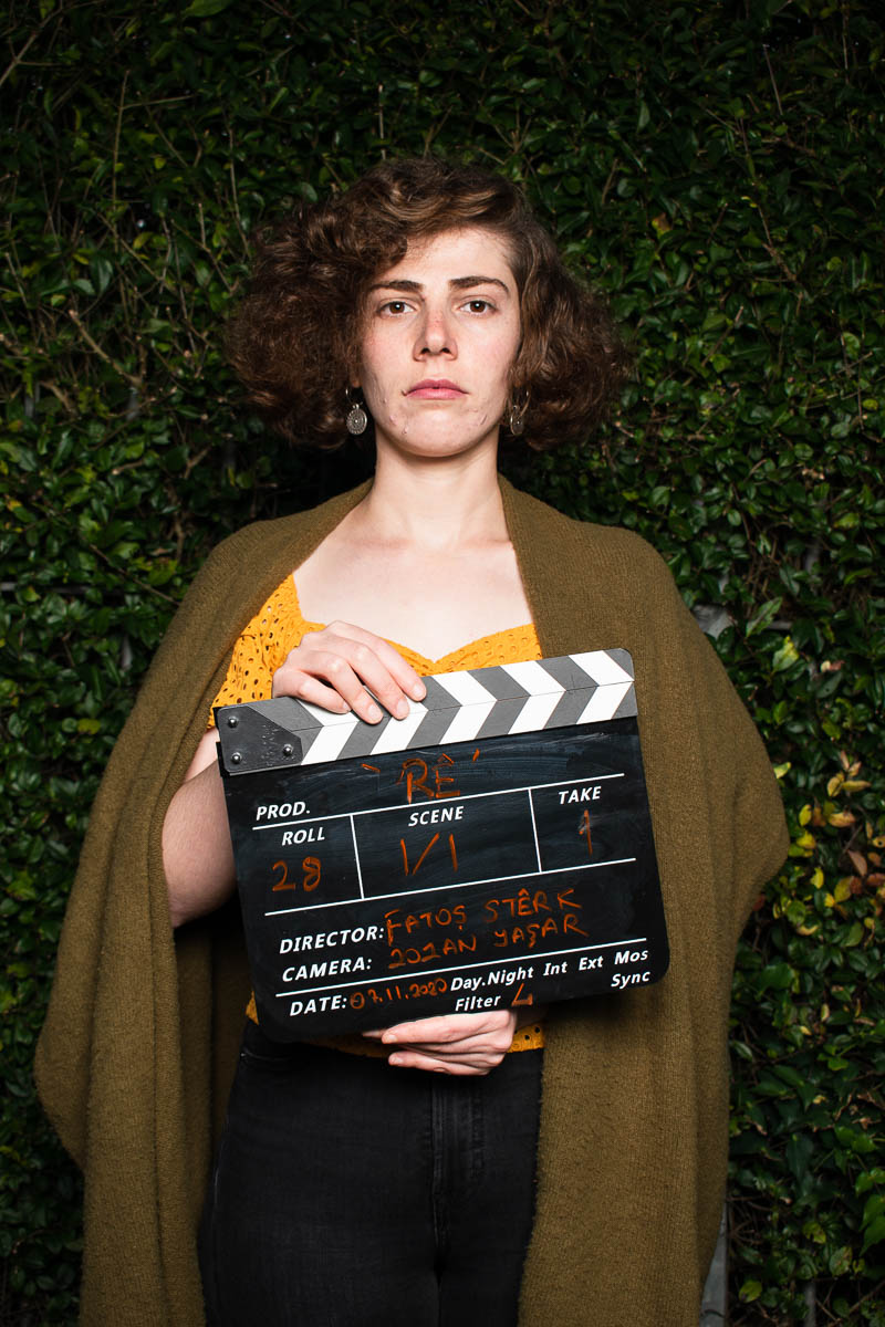 Portrait of refugee Fatos wearing a woolen shrug and holding a clapperboard
